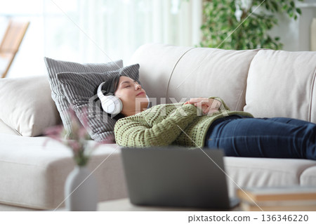 Asian woman doing audiotherapy lying on a couch at home 136346220
