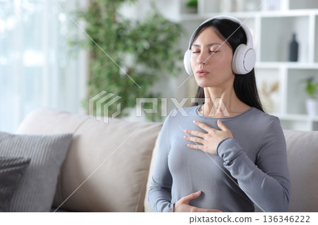 Asian woman doing guided breathing exercises at home Asian woman doing guided breathing exercises at home 136346222