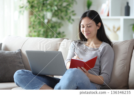 Asian woman taking notes in agenda using laptop Asian woman taking notes in agenda using laptop 136346235