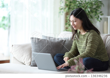Asian woman using laptop on a sofa in apartment interior Asian woman using laptop on a sofa in apartment interior 136346236