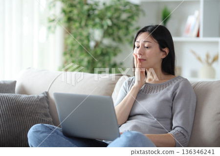 Disgusted asian woman checking mistakes on laptop at home Disgusted asian woman checking mistakes on laptop at home 136346241