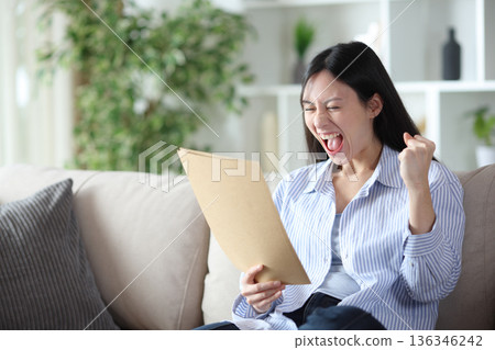 Excited asian woman at home checking documents 136346242