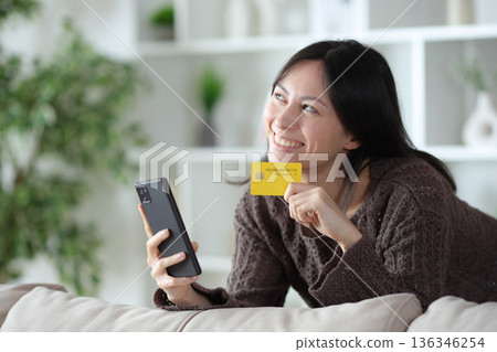 Happy asian woman holding credit card and thinking 136346254