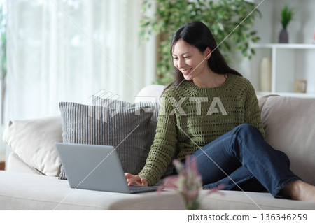 Happy asian woman using personal computer at home Happy asian woman using personal computer at home 136346259