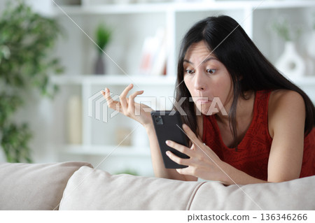 Perplexed asian woman checking strange news on phone Perplexed asian woman checking strange news on phone 136346266