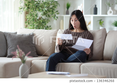 Surprised asian woman reading letter at home Surprised asian woman reading letter at home 136346268