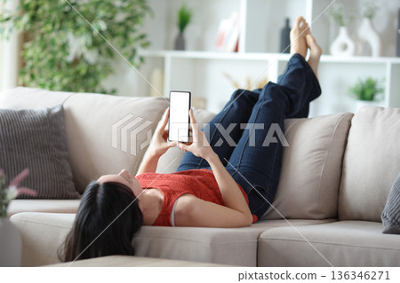 Woman lying on a couch using phone with blank screen 136346271