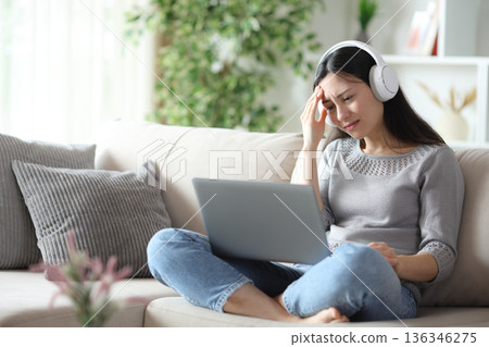 Worried asian woman wearing headphone is checking laptop 136346275