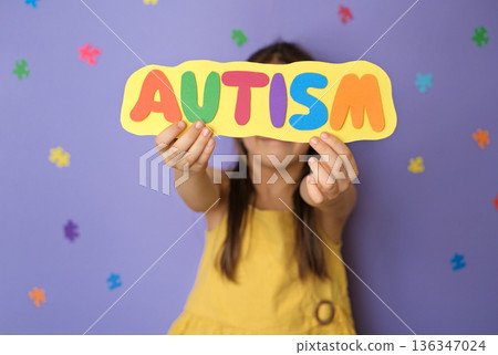 Child holding colorful autism sign on purple background. Inclusive education, learning diversity, school support, acceptance, awareness and educational inclusion concept. Child holding colorful autism sign on purple background. Inclusive education, learning diversity, school support, acceptance, awareness and educational inclusion concept. 136347024