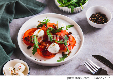 Caprese salad with tomatoes, mozzarella and arugula on a plate on the table Caprese salad with tomatoes, mozzarella and arugula on a plate on the table 136347506