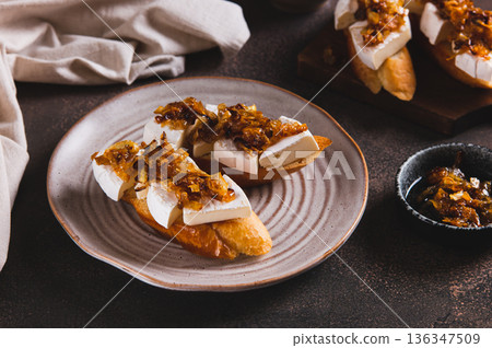 Toasts with creamy brie cheese and caramelized onions on a plate on the table 136347509