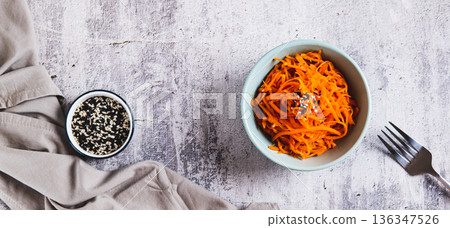 Spicy Korean carrots with sesame seeds in a bowl on the table top view web banner 136347526