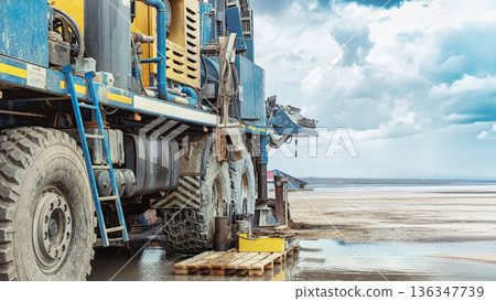 A drilling rig is positioned near the shoreline. Workers manage the rig as it extracts oil and gas resources. The weather shows cloudy skies and water nearby A drilling rig is positioned near the shoreline. Workers manage the rig as it extracts oil and gas resources. The weather shows cloudy skies and water nearby 136347739