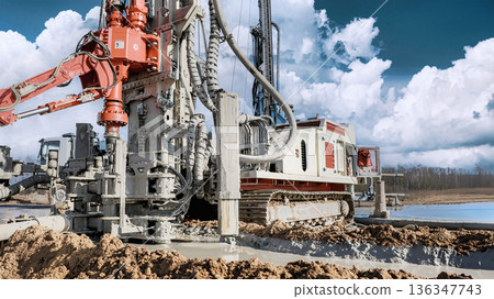 A drilling rig is actively working on a site, drilling into the ground for oil and gas resources while large clouds float overhead on a clear day A drilling rig is actively working on a site, drilling into the ground for oil and gas resources while large clouds float overhead on a clear day 136347743