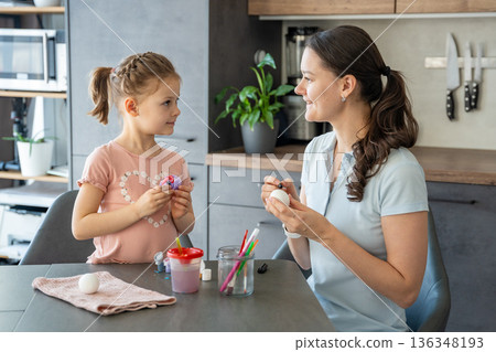 Little girl decorating Easter egg using brush and vivid colors. A moment of childhood joy and focus on holiday traditions. Little girl decorating Easter egg using brush and vivid colors. A moment of childhood joy and focus on holiday traditions. 136348193