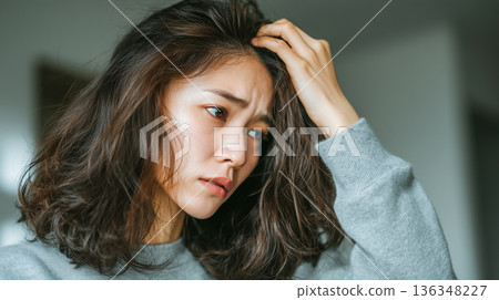 一位年輕女子因脫髮和頭髮受損而神情嚴肅。 136348227