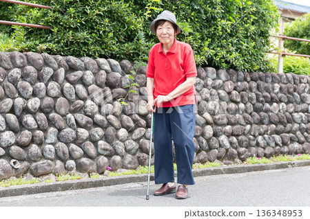 Senior woman walking on the road outdoors using a cane, whole body 136348953