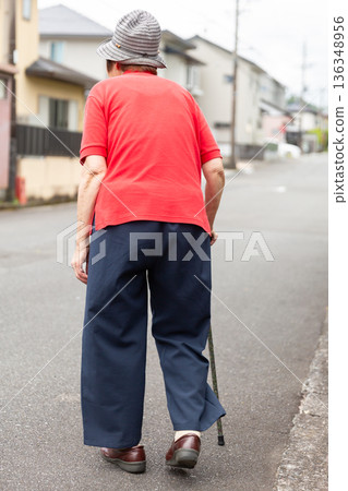 Back view of a senior woman walking outdoors with a cane. Full body image of elderly people. 136348956