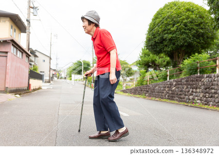 一位老年婦女拄著拐杖在戶外道路上行走，側視圖，全身照 136348972