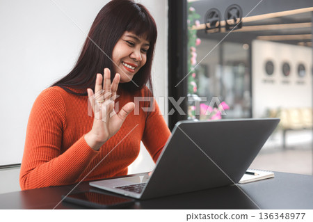 Happy Asian woman waving hand during video call on laptop in cafe. Smiling businesswoman working remote, online meeting, digital nomad lifestyle and telecommunication concept. Happy Asian woman waving hand during video call on laptop in cafe. Smiling businesswoman working remote, online meeting, digital nomad lifestyle and telecommunication concept. 136348977