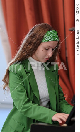 A female pianist in a stylish green suit performs a classical piece, showcasing her skill and commitment to the art. The soft lighting adds warmth and character to the performance. 136350728