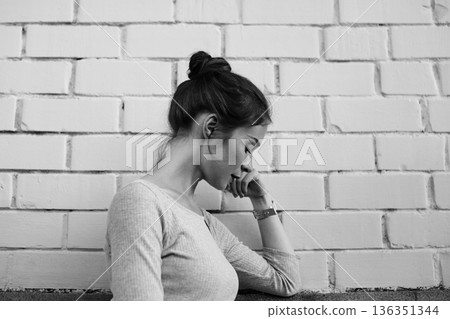 White Woman Seated Against Brick Wall, Pensive Writer Sketching Thoughts, Monochrome Mood, Soft Side Lighting, Textured Background, Casual Top And Bun, Intimate Contemplative Atmosphere, Urban Minimal 136351344