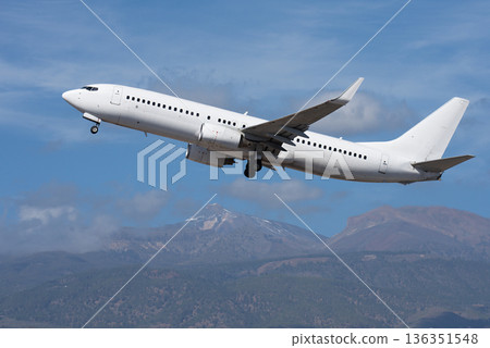 Airplane take off on the blue sky, with white clouds. Aircraft flying on sky background. White passenger jet plane in the blue sky. In the background the volcano el Teide Airplane take off on the blue sky, with white clouds. Aircraft flying on sky background. White passenger jet plane in the blue sky. In the background the volcano el Teide 136351548