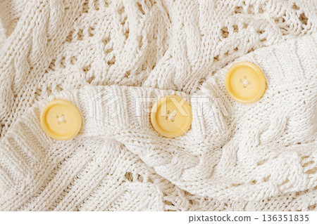 White knitted pullover fabric with cable knit pattern, round buttons close-up, clothing detail, fashion, textile background. Concept of knitwear comfort, clothing design, fabric texture, copy space White knitted pullover fabric with cable knit pattern, round buttons close-up, clothing detail, fashion, textile background. Concept of knitwear comfort, clothing design, fabric texture, copy space 136351835
