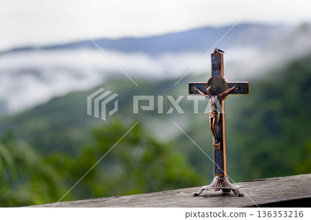 A solitary wooden holy cross standing outdoors against soft green hills and misty natural background conveying faith spirituality and calm reflection. A solitary wooden holy cross standing outdoors against soft green hills and misty natural background conveying faith spirituality and calm reflection. 136353216