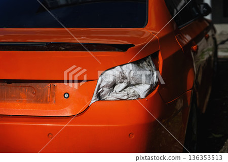 Damaged rear section of orange passenger car with broken taillight, visible impact deformation. Vehicle accident damage, insurance claim documentation, auto repair service, transportation safety 136353513