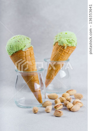 Two pistachio ice cream cones in glass jars with nuts on light textured background 136353641
