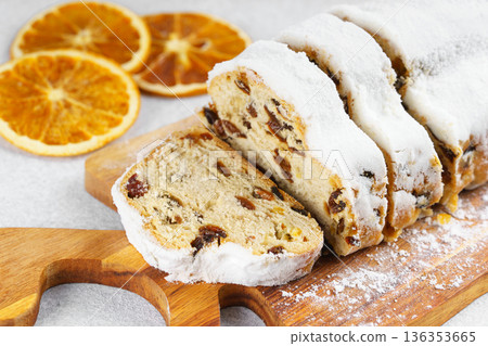 Traditional sliced Christmas stollen loaf with raisins and powdered sugar on wooden cutting board 136353665