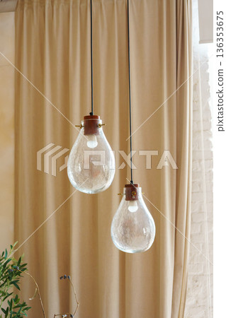 Handmade glass pendant lights hanging in minimalist interior space on beige curtains background 136353675