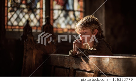 Young boy prayer sits alone at old wooden bench inside a rustic church. 136353779