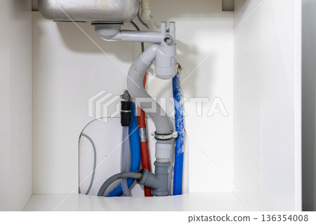 Modern kitchen sink plumbing system with exposed grey drainage pipes and colorful water supply lines, illustrating essential home utility piping and maintenance Modern kitchen sink plumbing system with exposed grey drainage pipes and colorful water supply lines, illustrating essential home utility piping and maintenance 136354008