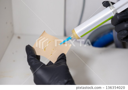 Person wearing black protective glove applying insecticidal gel from a tube onto paper for effective pest control or professional home extermination service Person wearing black protective glove applying insecticidal gel from a tube onto paper for effective pest control or professional home extermination service 136354020