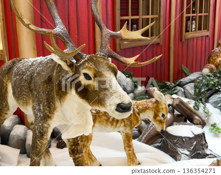 Large deer and small fawn statues, covered in artificial snow, creating a festive winter wonderland scene for holiday retail displays and seasonal decoration Large deer and small fawn statues, covered in artificial snow, creating a festive winter wonderland scene for holiday retail displays and seasonal decoration 136354271