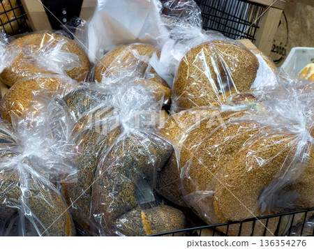 Artisanal freshly baked bread loaves, topped with sesame and poppy seeds, individually wrapped in clear plastic bags for hygienic supermarket retail display Artisanal freshly baked bread loaves, topped with sesame and poppy seeds, individually wrapped in clear plastic bags for hygienic supermarket retail display 136354276
