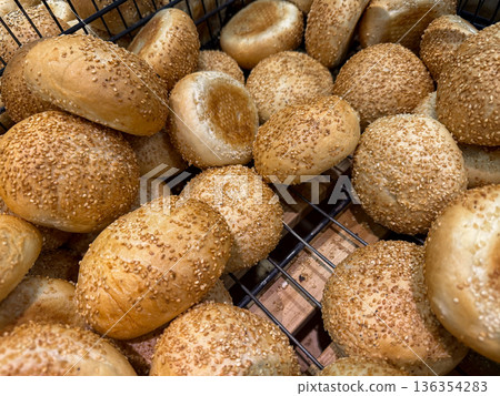 Freshly baked golden brown sesame seed buns piled in a wire basket, symbolizing delicious breakfast food and bakery product availability for daily meal options Freshly baked golden brown sesame seed buns piled in a wire basket, symbolizing delicious breakfast food and bakery product availability for daily meal options 136354283
