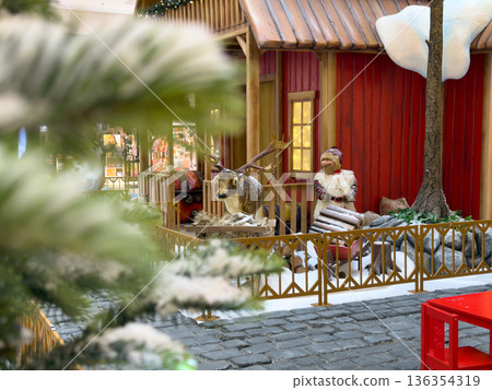 Detailed Christmas display featuring a charming red house, festive reindeer statue, and a cozy Santa figure, creating a joyful holiday shopping atmosphere in a retail mall Detailed Christmas display featuring a charming red house, festive reindeer statue, and a cozy Santa figure, creating a joyful holiday shopping atmosphere in a retail mall 136354319