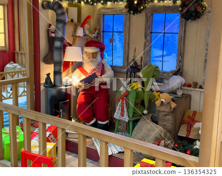Santa Claus figurine diligently reading a book in a cozy, festive Christmas display, surrounded by an elf, gifts, and snowy windows, symbolizing holiday preparation Santa Claus figurine diligently reading a book in a cozy, festive Christmas display, surrounded by an elf, gifts, and snowy windows, symbolizing holiday preparation 136354325
