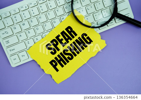 Yellow paper with text "Spear Phishing" and magnifying glass placed on a white keyboard Yellow paper with text "Spear Phishing" and magnifying glass placed on a white keyboard 136354664