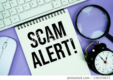 Notepad with the text "Scam Alert!" and white keyboard, wireless mouse, magnifying glass and alarm clock Notepad with the text "Scam Alert!" and white keyboard, wireless mouse, magnifying glass and alarm clock 136354671