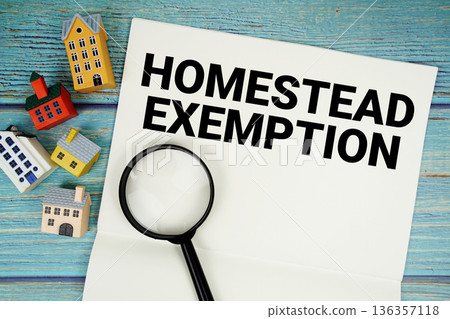 Notepad with "Homestead Exemption" with magnifying glass and house model on wooden background Notepad with "Homestead Exemption" with magnifying glass and house model on wooden background 136357118