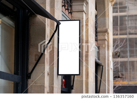 Blank vertical signboard mockup hanging on an old building stone facade, advertising banner template for storefront branding in a city street 136357160