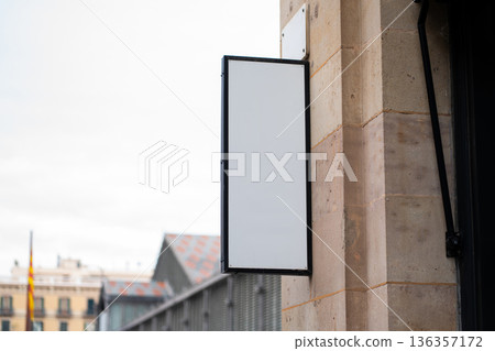 Blank vertical outdoor shop signage mockup showcasing a clean white display on a stone building in an urban street, providing space for branding and advertising Blank vertical outdoor shop signage mockup showcasing a clean white display on a stone building in an urban street, providing space for branding and advertising 136357172