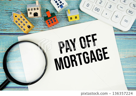 Notepad with "Pay Off Mortgage" with Calculator, magnifying glass and house model on wooden background 136357224