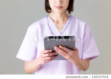 A middle-aged female nurse wearing a medical scrub holding a tablet A middle-aged female nurse wearing a medical scrub holding a tablet 136357458
