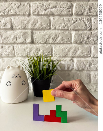 A woman's hand inserts a matching shaped figure into a wooden puzzle. multicolored wooden puzzle on a white background A woman's hand inserts a matching shaped figure into a wooden puzzle. multicolored wooden puzzle on a white background 136358099