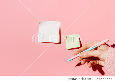 Hand with pen and sticky notes on pink background, copy space 136358367
